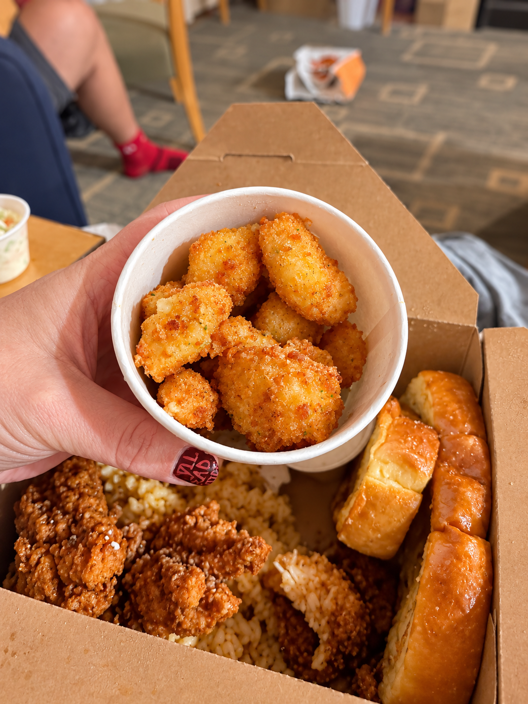 Small white cup of golden fried cheese curds held above our Big Chicken takeout meal