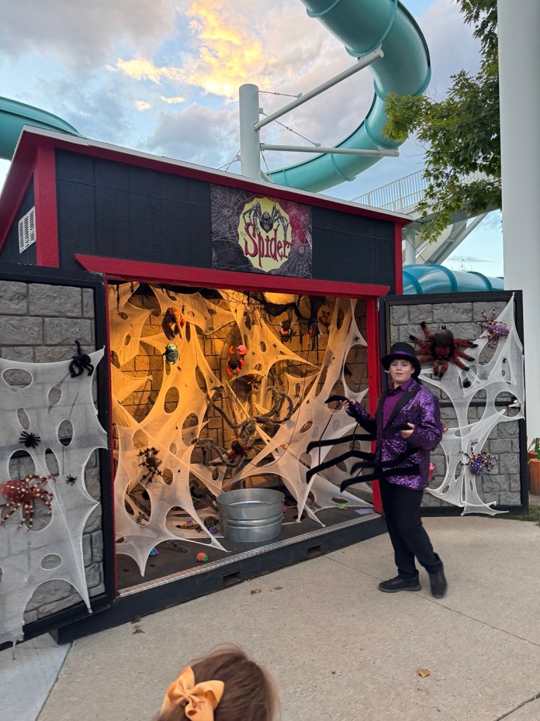 Spider-themed Treat Street booth with cobwebs, spider decorations and a costumed attendant at Lagoon Frightmares.