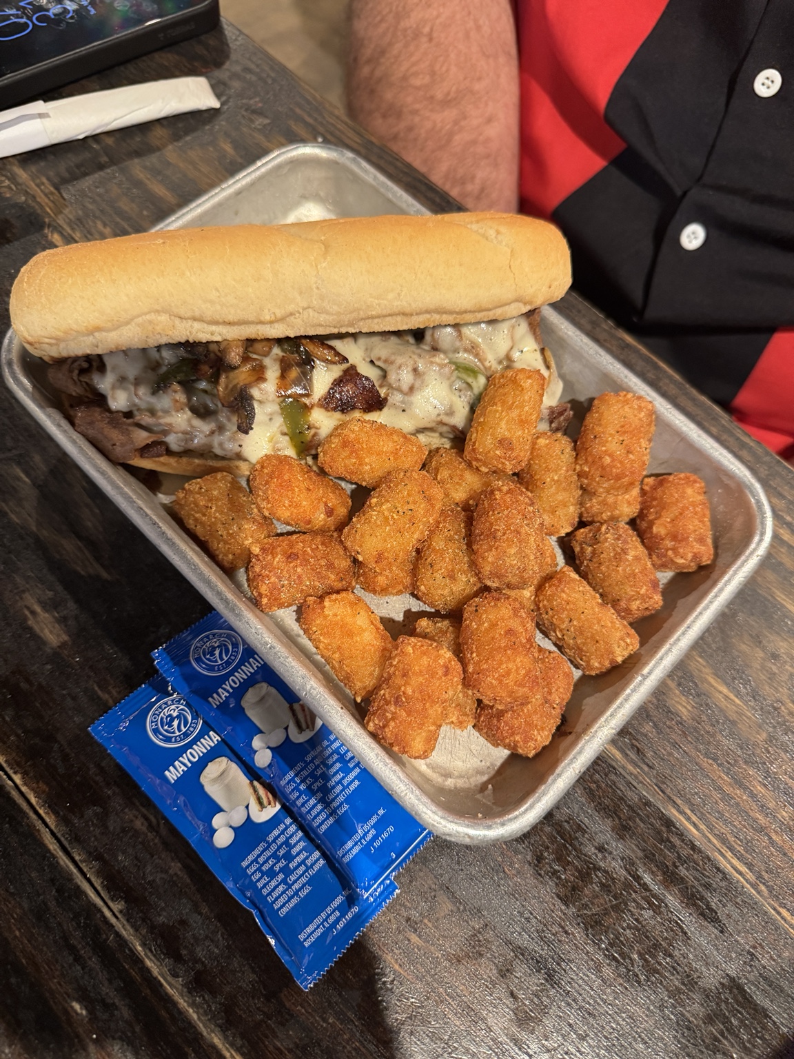 Cheesesteak sandwich with melted cheese, grilled peppers and onions, and a generous side of tater tots