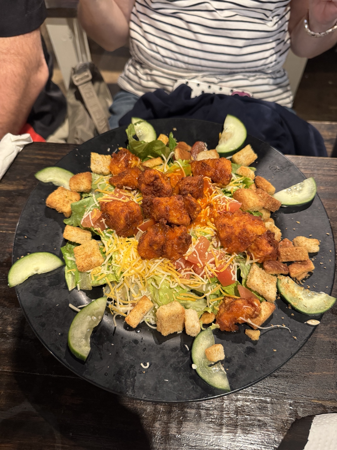 Large salad topped with crispy sauced chicken, shredded cheese, tomatoes, cucumbers, and croutons