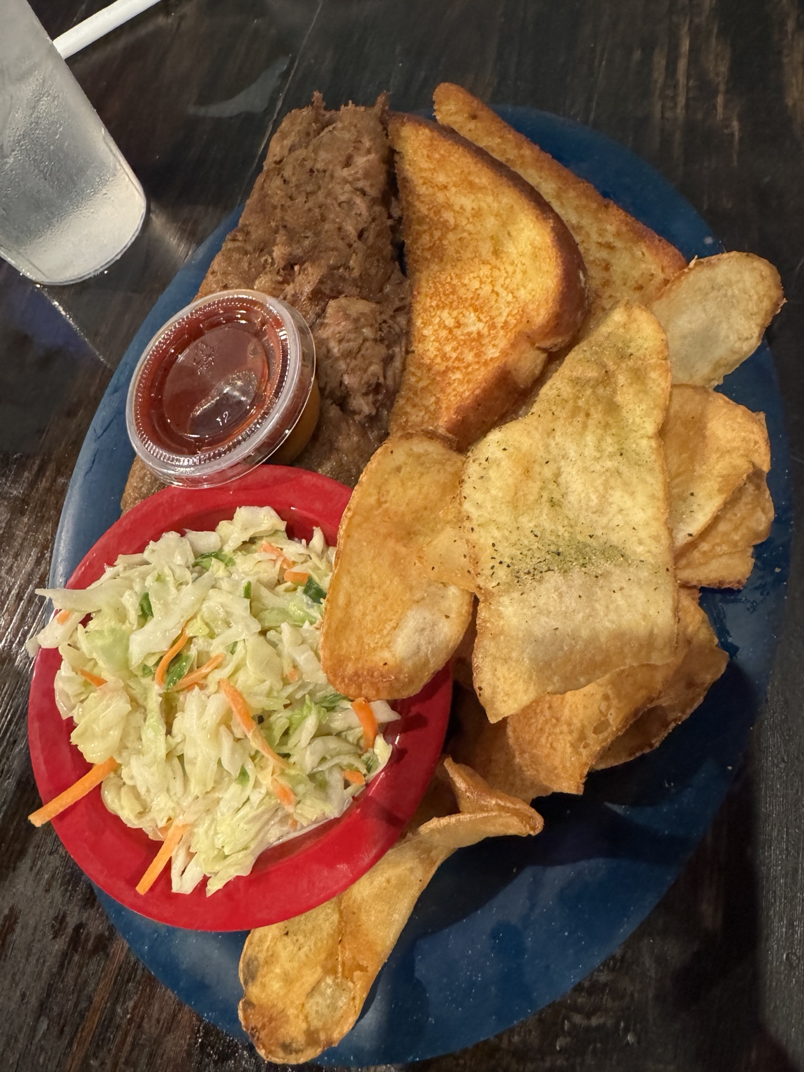 Hearty meat sandwich with toasted bread, potato chips, coleslaw, and a cup of sauce