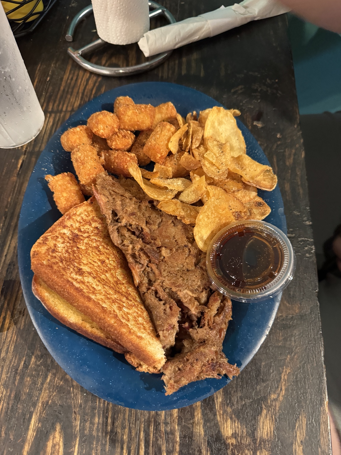Toasted meat-filled sandwich served with tater tots, chips, and a cup of dipping sauce
